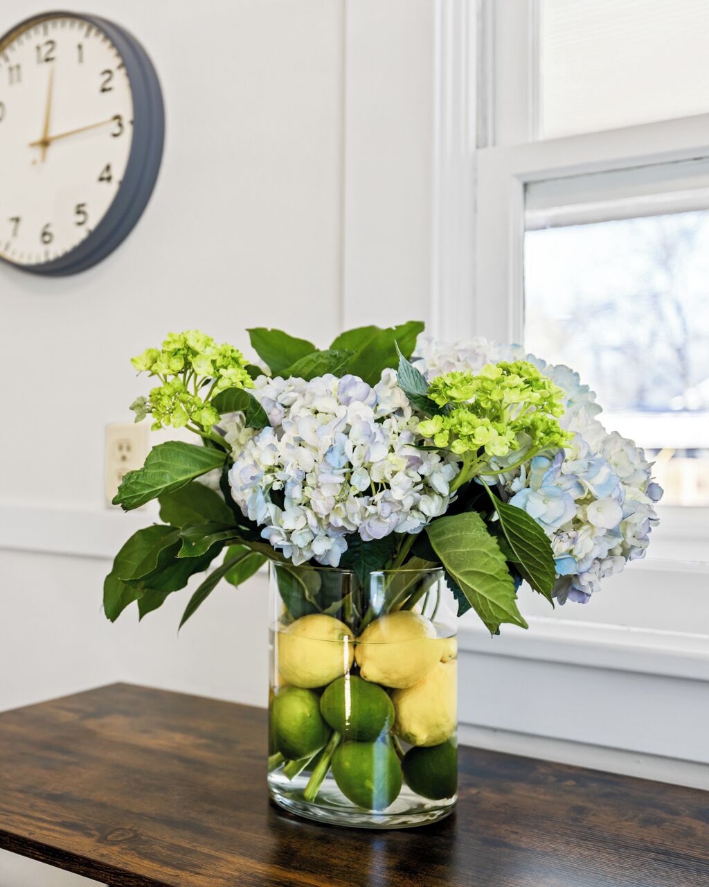 A vase with flowers and lemons on a wooden table.