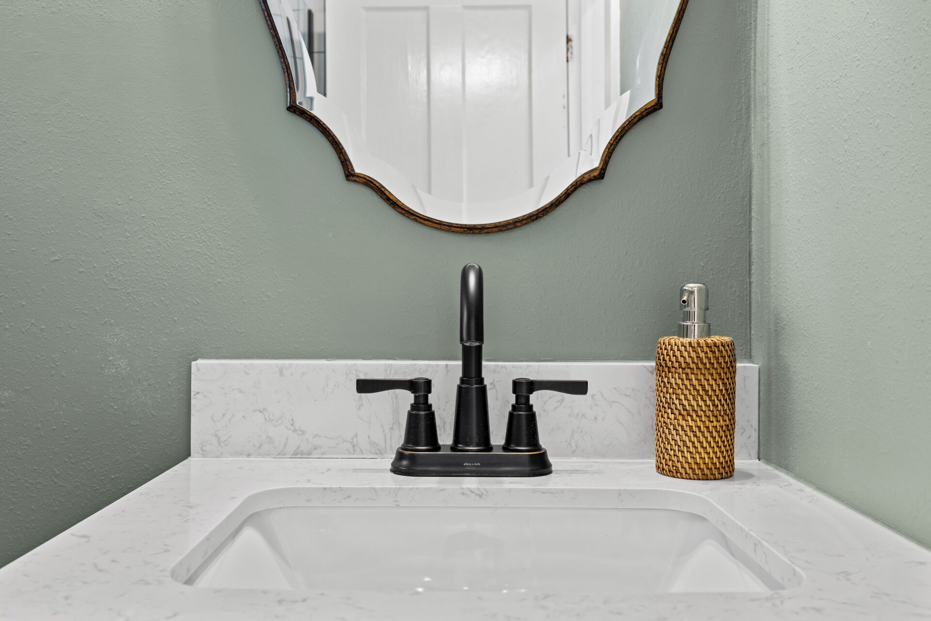 A bathroom with a white sink, black faucet, and a woven soap dispenser.