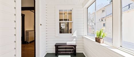 A narrow hallway with a bench, a large window with a view of buildings, and a door leading to another room.