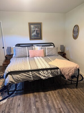 A bed with a patterned bedspread, pillows, and a blanket. There are two bedside tables with lamps. A framed picture hangs on the wall above the bed.