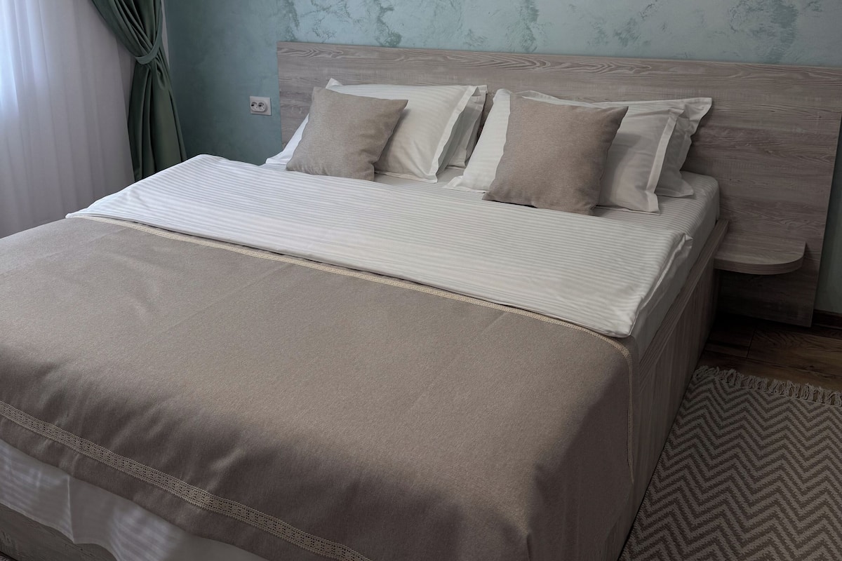 Un lit bien fait, avec une couverture et des oreillers de couleur beige, une tête de lit en bois et un tapis à motifs sur le sol.