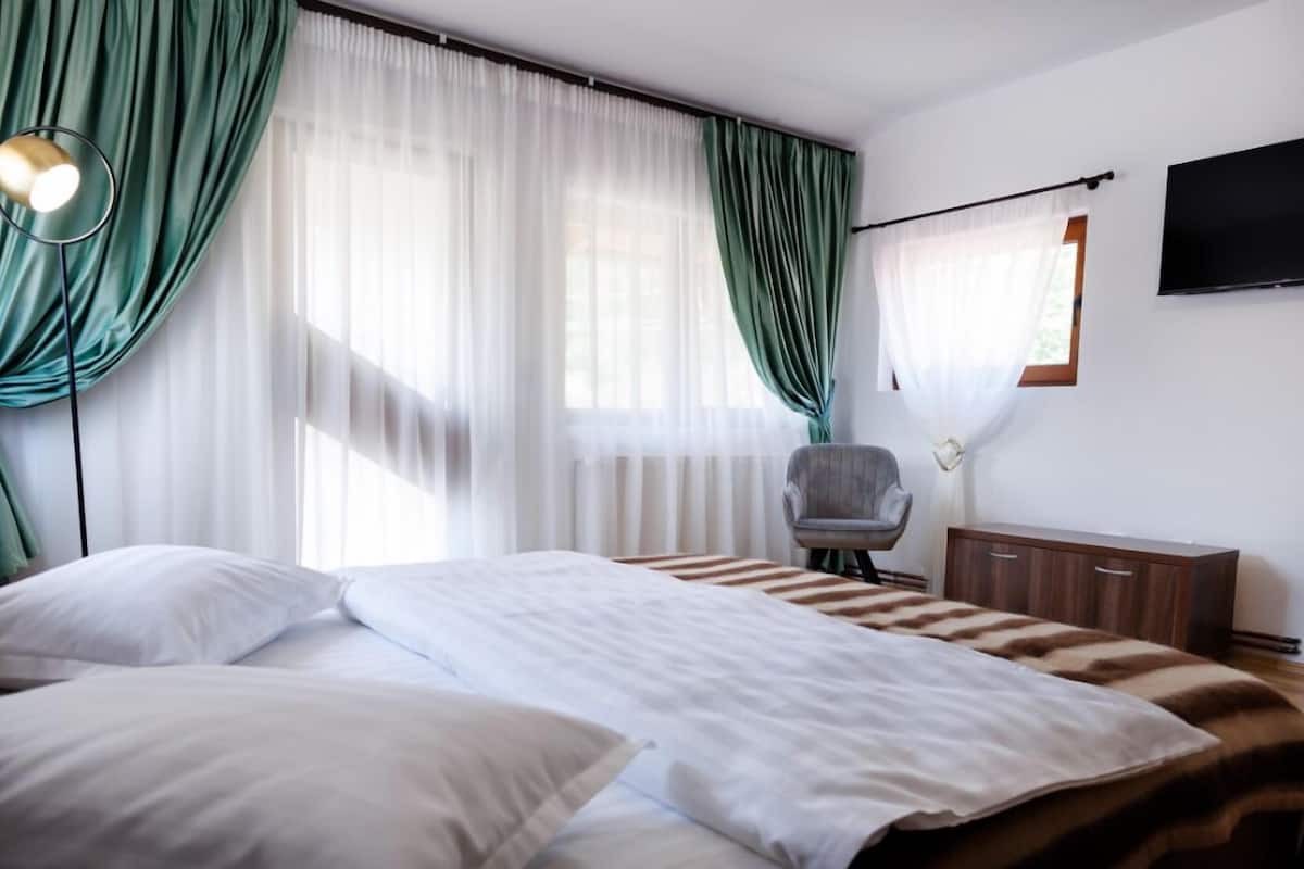Une chambre d’hôtel avec un lit, une chaise, une télévision et une fenêtre avec des rideaux.
