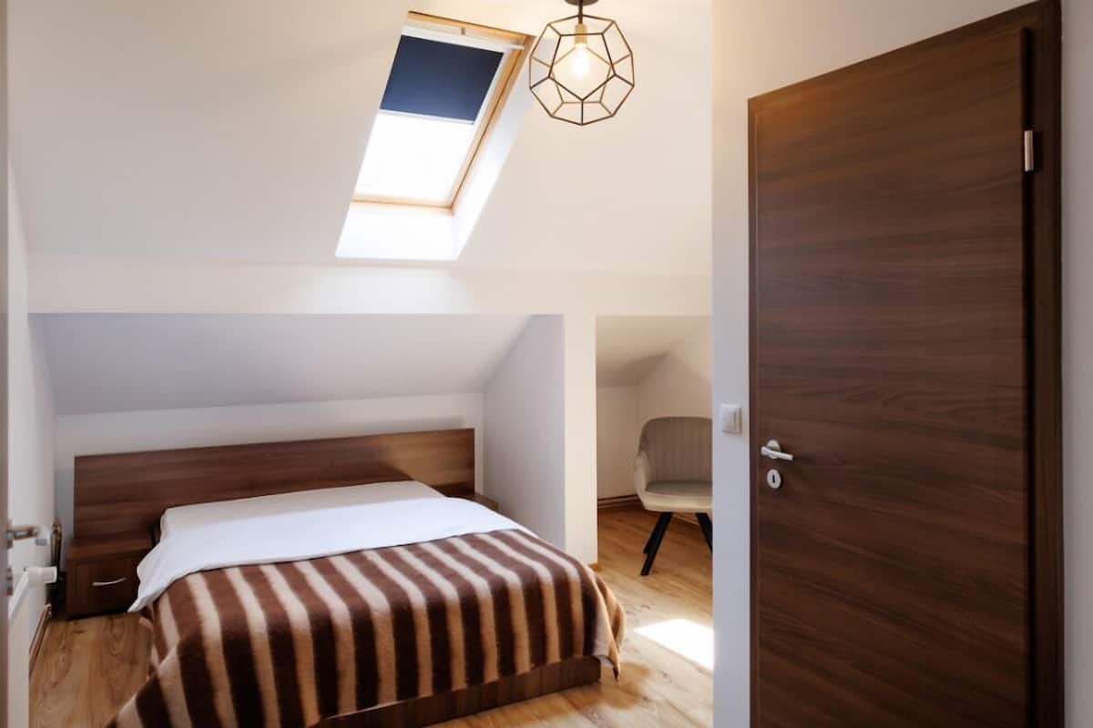Une chambre avec un puits de lumière, une porte en bois, un lit avec une literie à rayures et une chaise.