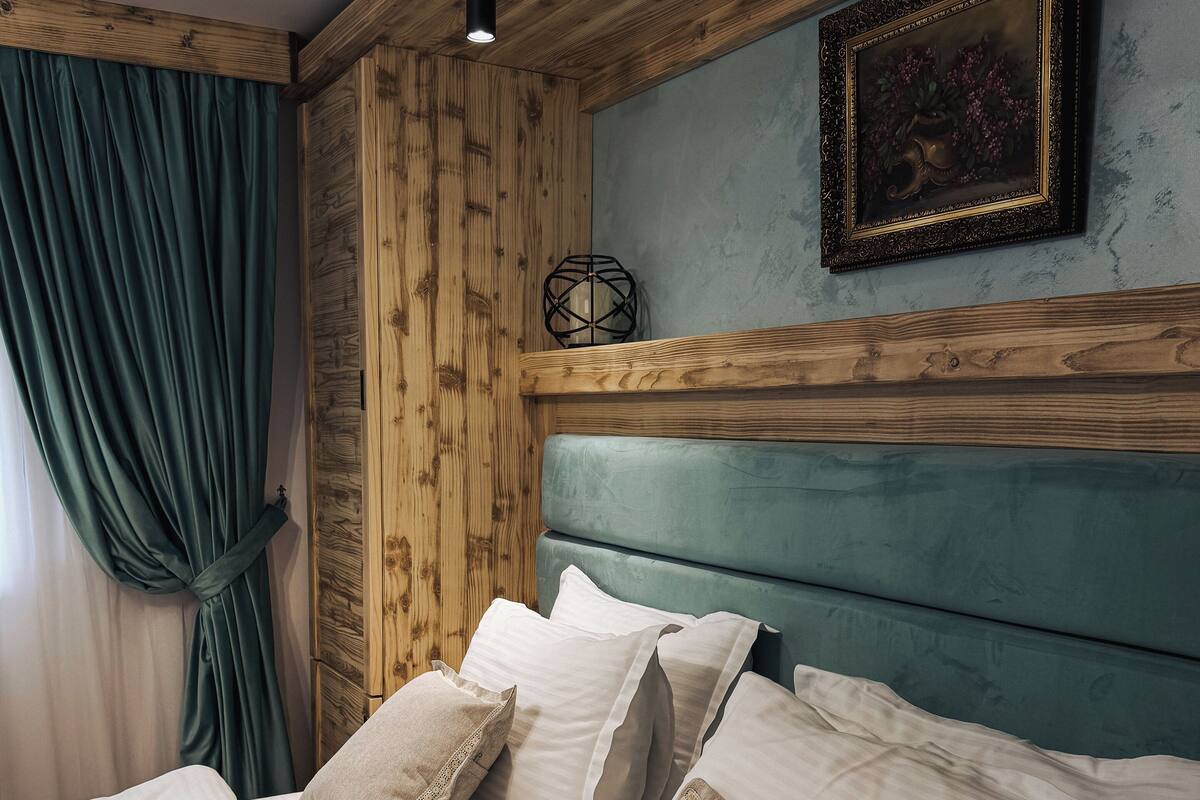 Un lit avec du linge de lit blanc et des oreillers beige, une tête de lit en bois, un mur de couleur turquoise et un tableau encadré au-dessus du lit.