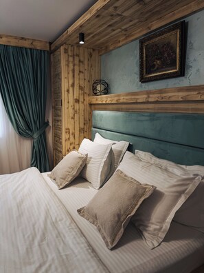 Ein Bett mit weißen Leinentüchern und beigen Kissen, ein Holz-Kopfteil, eine türkisblaue Wand und ein gerahmtes Bild über dem Bett.