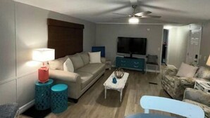 A modern living room with a sofa, a coffee table, a TV, and a ceiling fan. - Let Freedom Ring! (Hampstead)