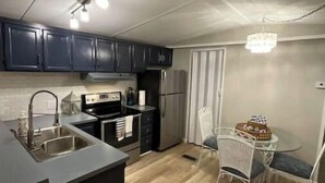 A modern kitchen with dark cabinets, stainless steel appliances, and a dining area with a glass table and white chairs. - Let Freedom Ring! (Hampstead)