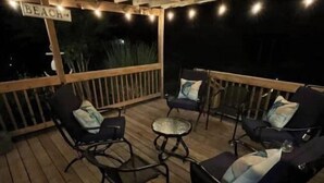 An outdoor deck with wooden flooring, metal chairs with cushions, and a small round table. - Let Freedom Ring! (Hampstead)