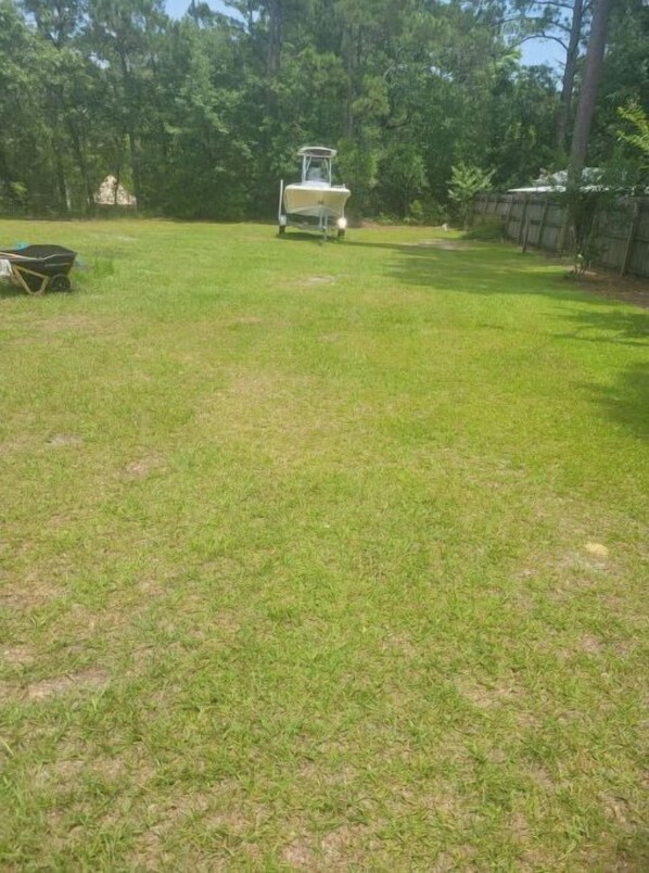 A grassy yard with a small boat and a wheelbarrow.