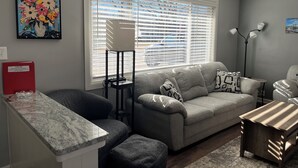 Un salon avec un canapé gris, une petite table basse, un lampadaire et un tableau accroché au mur.