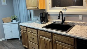 Une cuisine avec des meubles en bois, un plan de travail en granit, un évier noir et une machine à café.