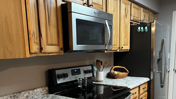 Une cuisine avec des meubles de rangement en bois, un réfrigérateur en acier inoxydable, un four à micro-ondes et un four traditionnel.