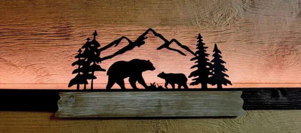 A silhouette of a bear, a cub, and trees against a wooden background.