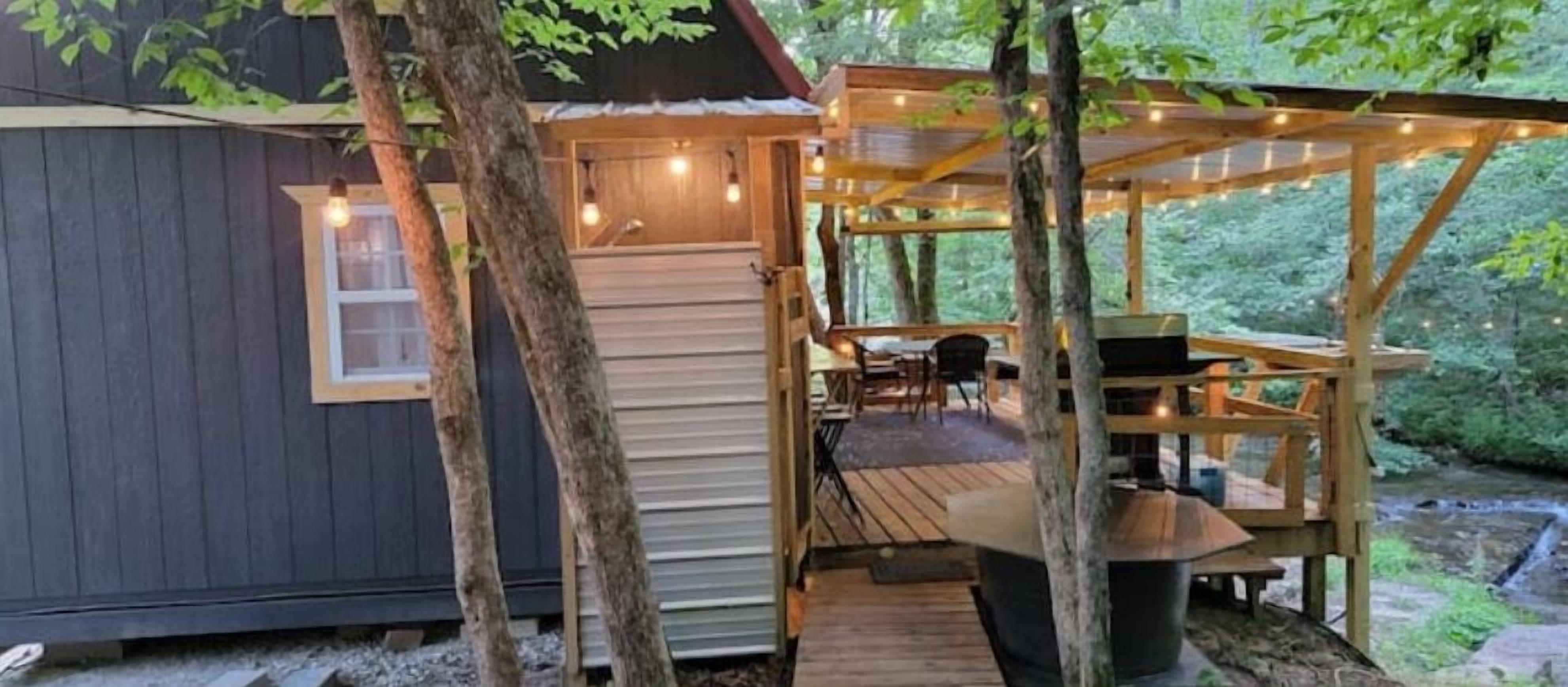 A cabin with a wooden deck, a small outdoor seating area, and a window overlooking the forest.