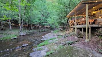A wooden cabin with a deck overlooking a stream in a forest.