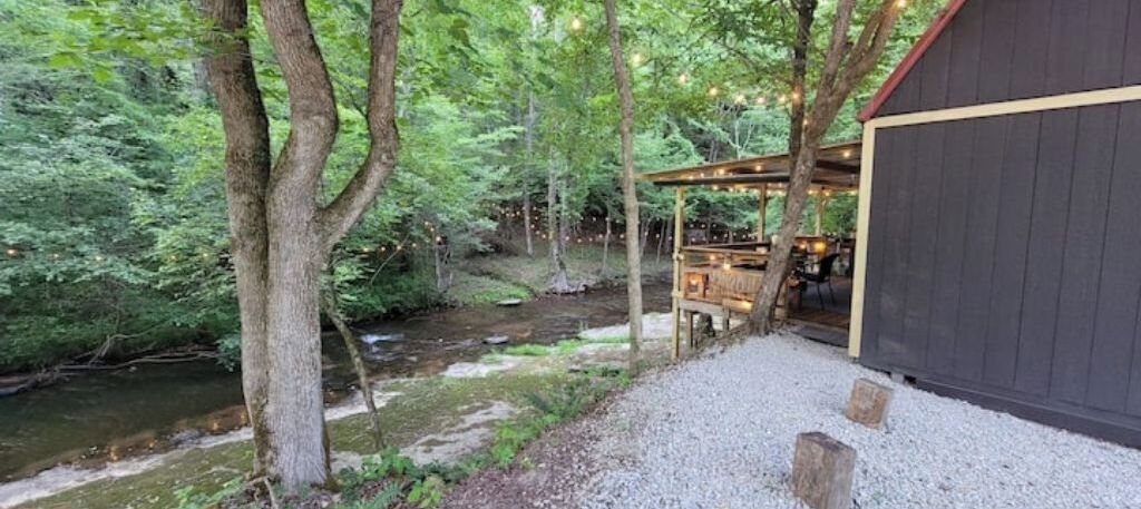 A rustic wooden building adjacent to a stream in a forested area.