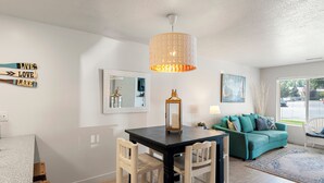 Un coin repas comprenant une table et des chaises, un luminaire suspendu, un miroir et un canapé vert donnant sur une fenêtre.