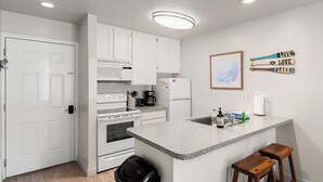 Une cuisine avec des meubles blancs, un four à micro-ondes, une cuisinière, un réfrigérateur, un plan de travail en granit, un évier et des tabourets en bois.