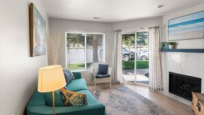Un salon avec un canapé de couleur turquoise, un lampadaire, une cheminée et une grande fenêtre ornée de rideaux à motifs.