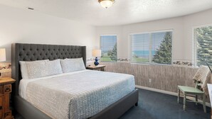 A bedroom with a large bed, a nightstand, a chair, and a window with blinds. - Condo - #310 | 2 Bed, 2 Bath (Garden City)