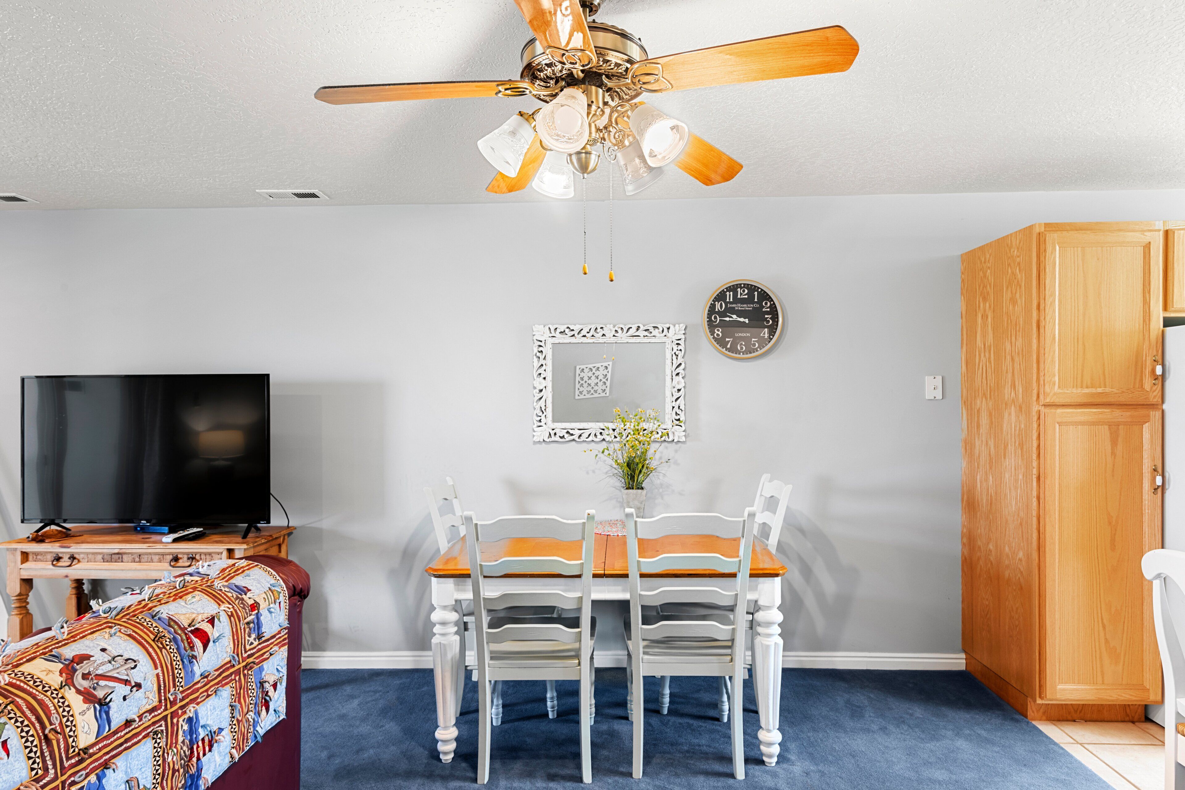 A living room with a ceiling fan, a TV, a dining table with chairs, a patterned sofa, and a wooden cabinet.