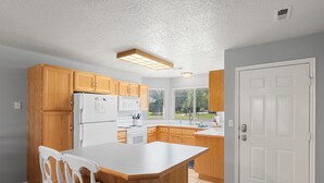 A kitchen with wooden cabinets, a white refrigerator, a microwave, and a large island. - Condo - #310 | 2 Bed, 2 Bath (Garden City)
