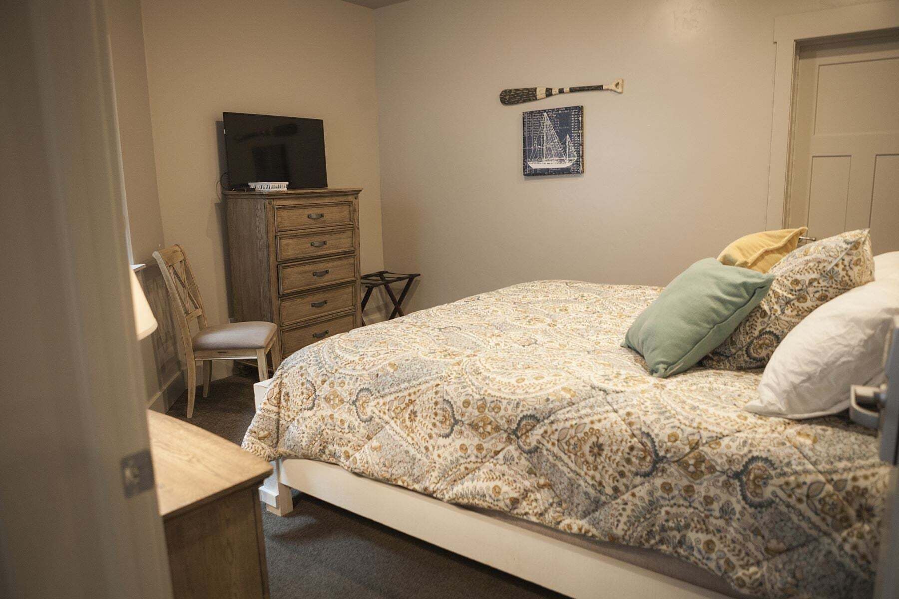 Un dormitorio con cama, cómoda, silla, televisor y un objeto fijado a la pared.