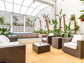 Een overdekt terras met rieten meubels, een zwembad en verschillende potplanten.