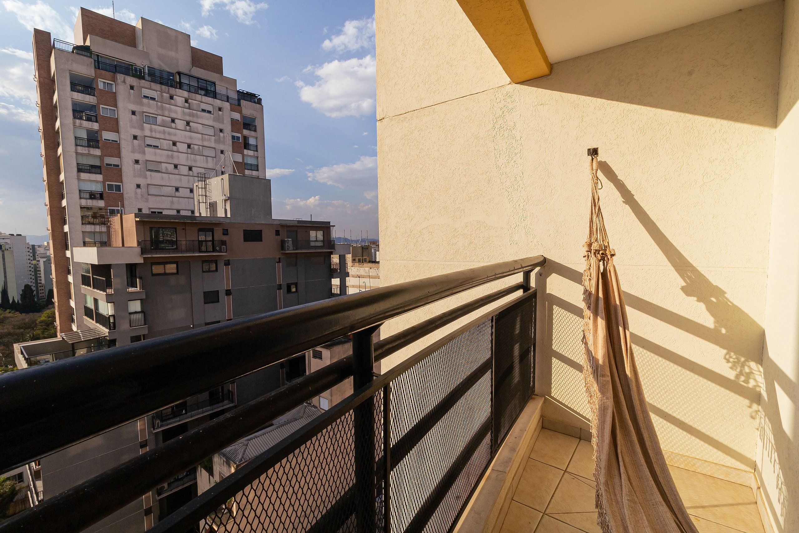 A balcony with a metal railing, a beige wall, and a view of a multi-story building in the background.