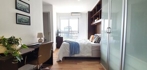 Un dormitorio con cama, escritorio, silla, planta y armario.