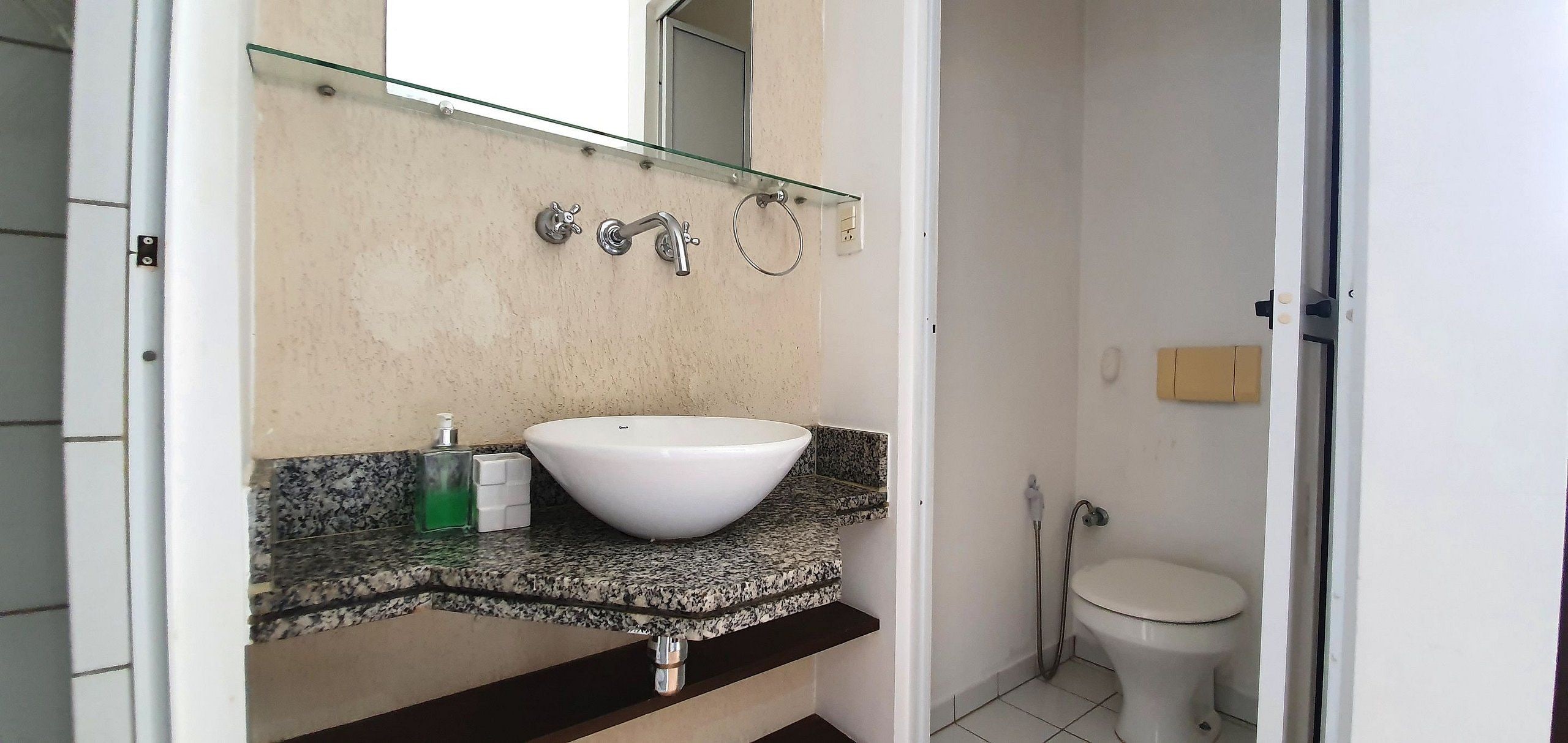 Un baño con lavamanos blanco, repisa de vidrio, espejo y retrete.