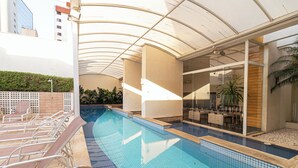 A swimming pool with lounge chairs, a covered area, and a view of a building in the background. - Vossa Bossa Bela Cintra Home (São Paulo)
