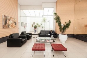 A modern reception area with black leather sofas, red ottomans, a glass coffee table, and a large potted plant.