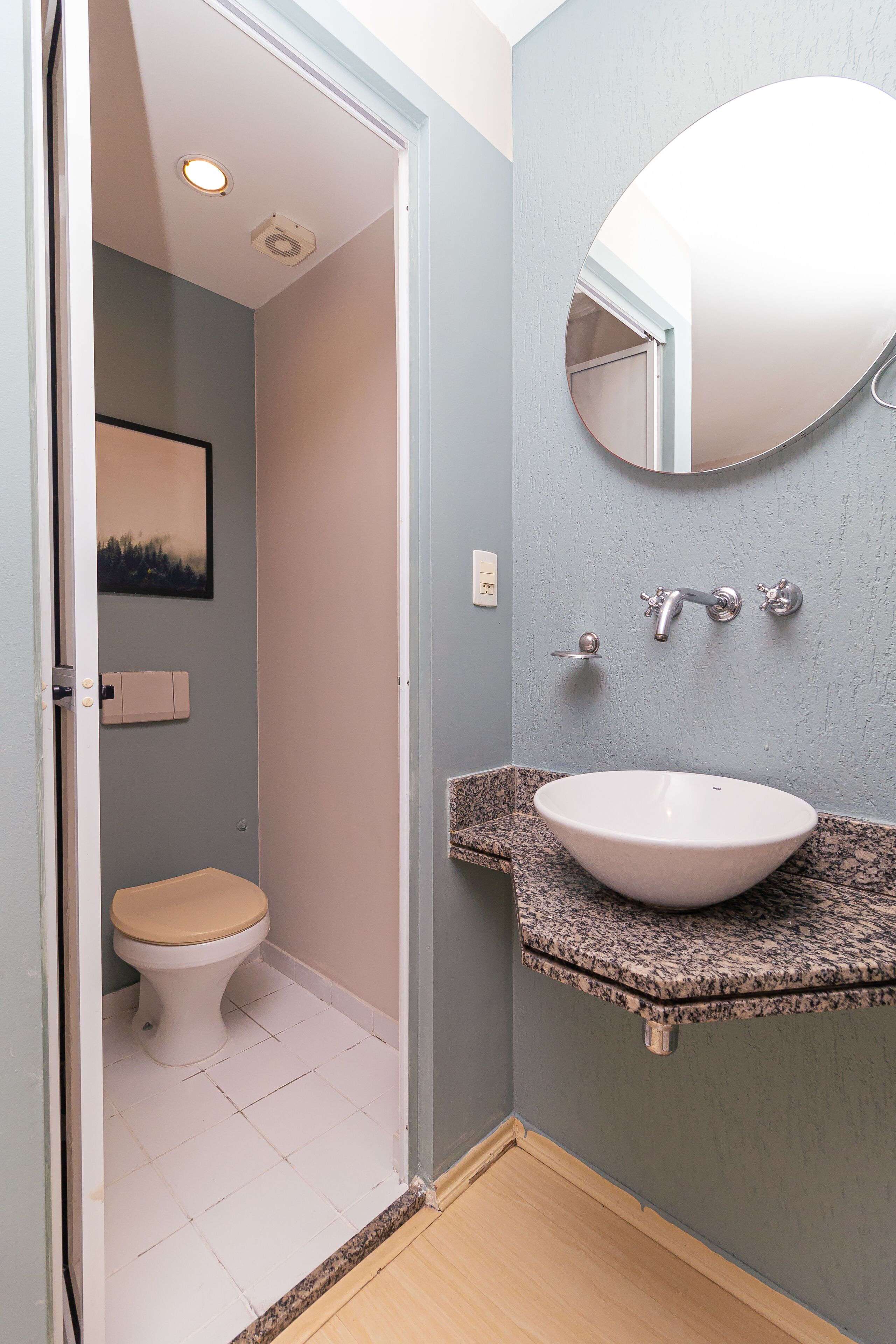 A bathroom with a white toilet, a granite countertop sink, a wall-mounted mirror, and a ceiling light.