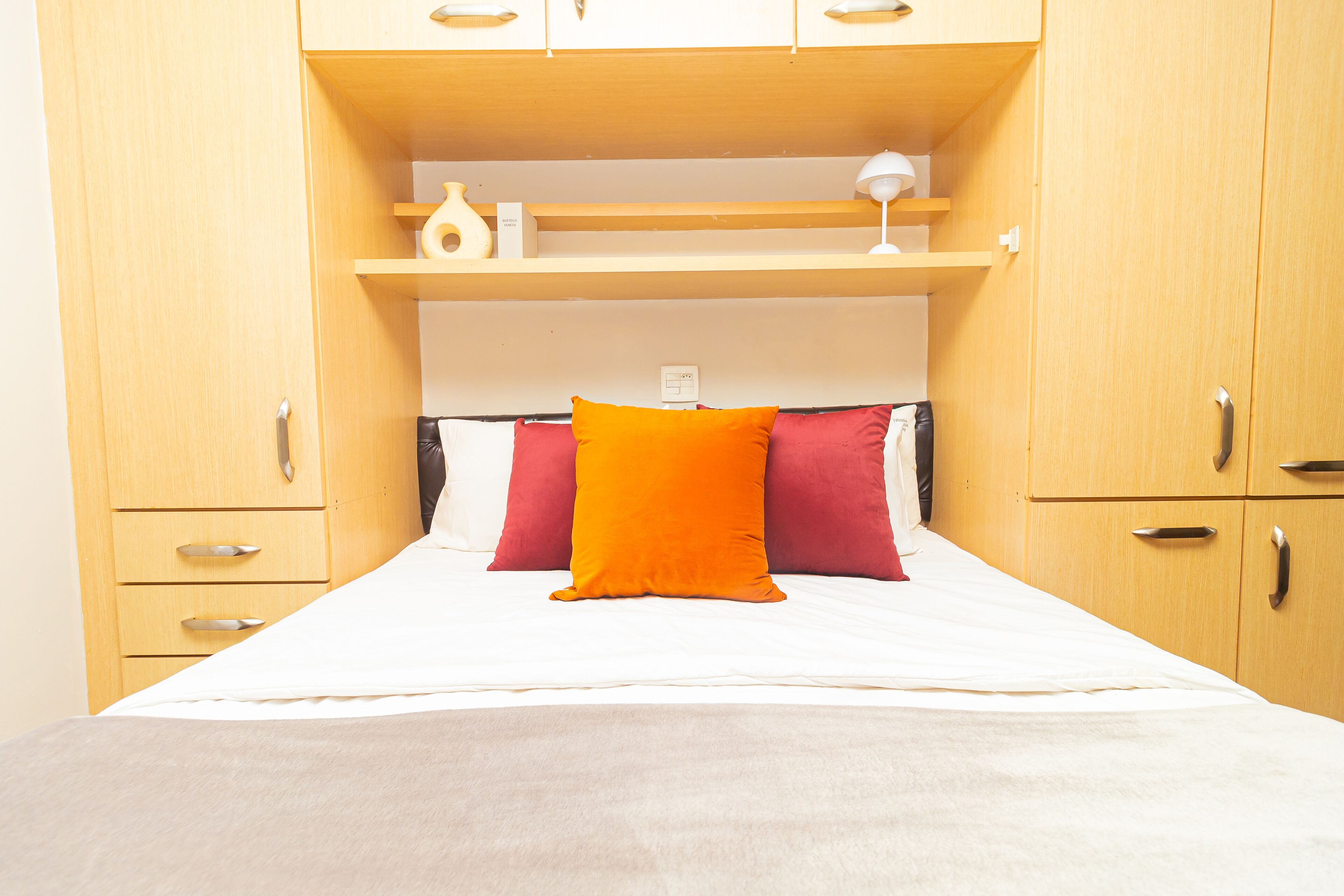 A bedroom with a bed, two pillows, a nightstand, and a shelf above the bed.