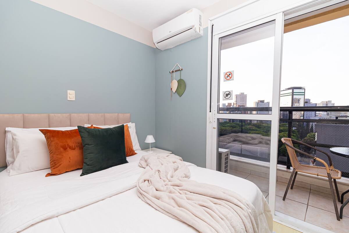 Une chambre d’hôtel avec un lit, des oreillers, une couverture, une table de chevet, une lampe et une vue sur la ville, visible à travers une porte coulissante.