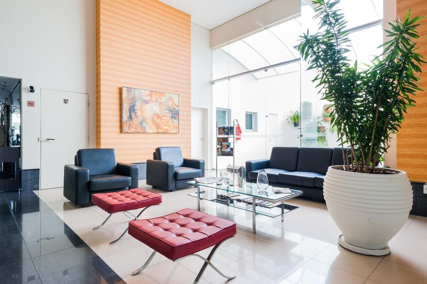 A modern lobby with seating, a large potted plant, and a painting on the wall.