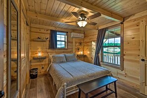 A wooden cabin bedroom with a bed, ceiling fan, and windows.