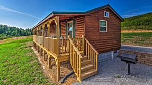 Une cabane en bois avec une véranda, des marches et un espace barbecue.