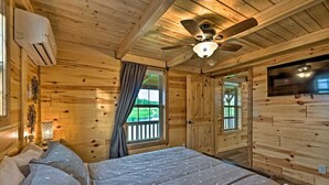 Une chambre dans un chalet en bois, avec un lit, un ventilateur de plafond et un téléviseur fixé au mur.
