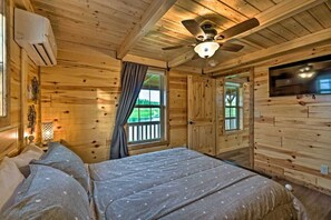 A wooden cabin room with a bed, ceiling fan, and a TV on the wall.