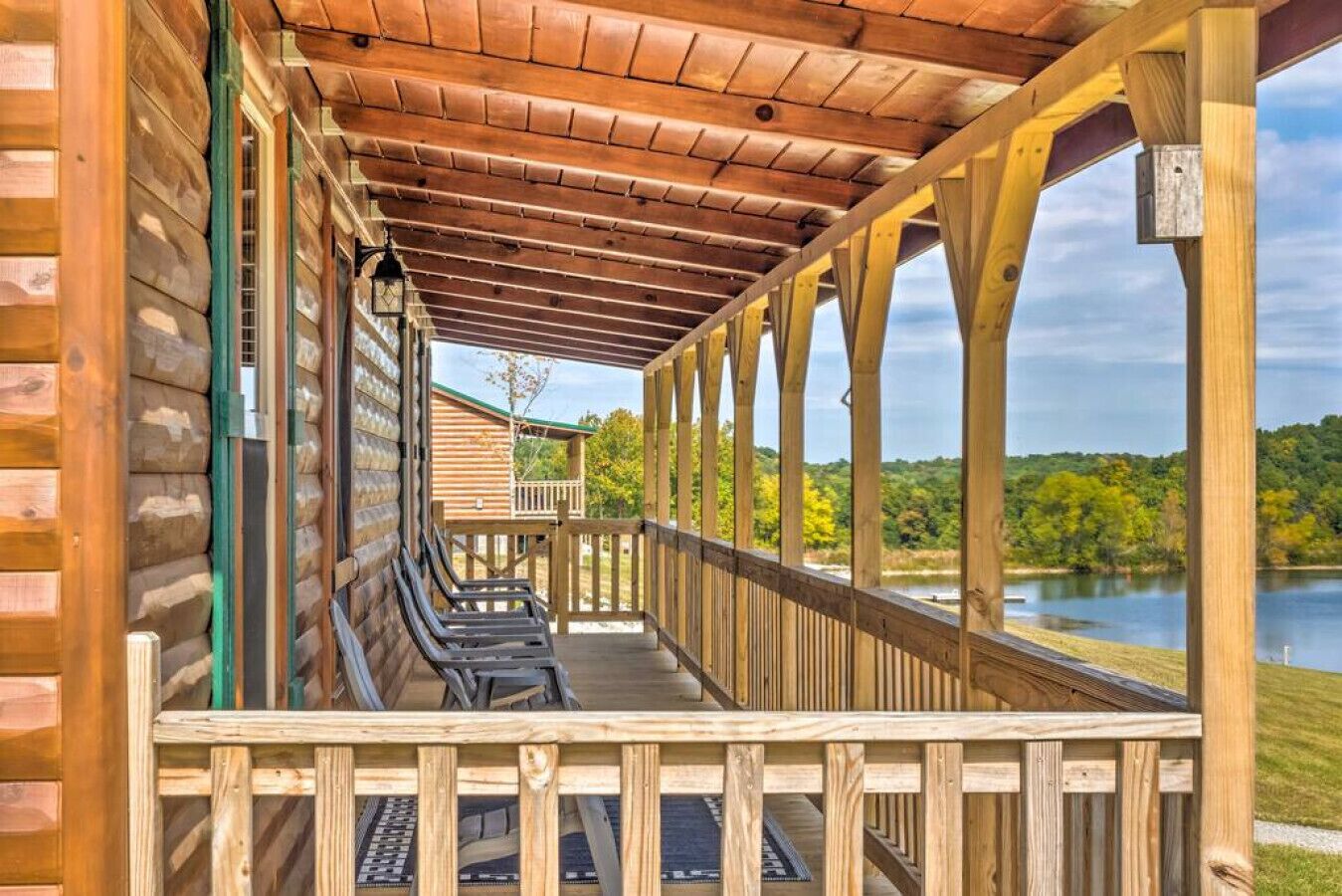 A covered outdoor seating area with benches, wooden railings, and a view of a lake.