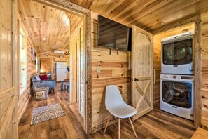Interior de una cabaña de madera con comedor, una silla blanca y un horno doble.