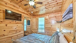 Ein Schlafzimmer einer Holzhütte mit Bett, Deckenventilator, Fernseher und Fenster.