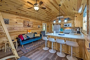 Ein Holzblockhaus mit Küchenzeile, einem blauen Sofa, einer Bar und einem Deckenventilator.