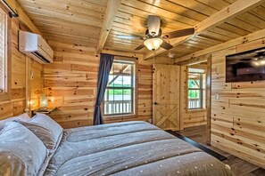 Une chambre de style cabane en bois, équipée d’un lit, d’un ventilateur de plafond, d’une télévision et d’une fenêtre avec des rideaux.
