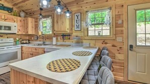 Interior de una cabaña de madera con una isla de cocina, armarios de madera, un microondas y una ventana con vista a follaje.