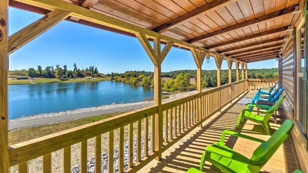 Una terraza techada con vistas a un lago, barandillas de madera y sillones reclinables verdes y azules.