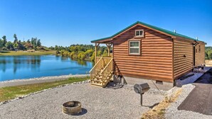 Una cabaña de madera con un porche, una fogata y vistas a un lago.