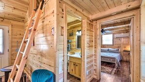 Interior de una cabaña de madera con cama, baño y comedor.